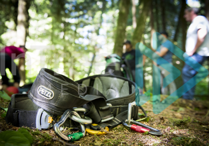 Climbing harness on the ground with crew meeting in background